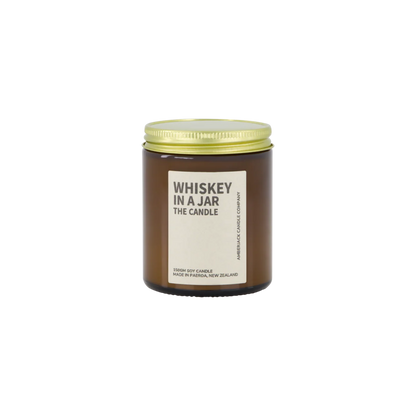 Amber glass jar with brass lid containing whiskey in a jar candle on white background. 