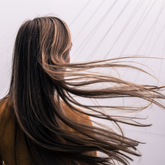 Back view of woman with long straight brown hair being swept in the wind. 