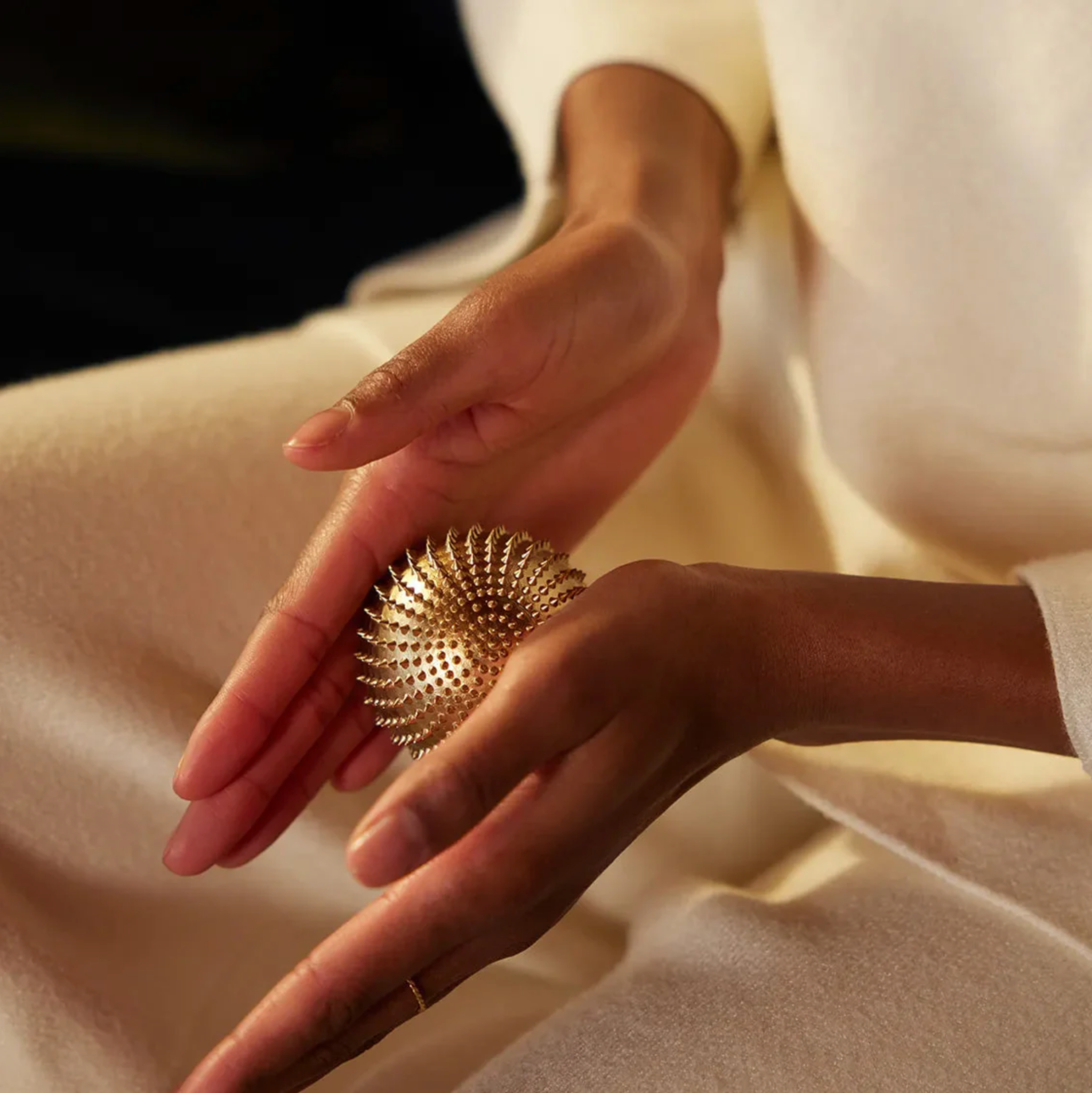 Close-up of hands holding a textured gold ball against a neutral background