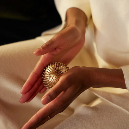 Close-up of hands holding a textured gold ball against a neutral background
