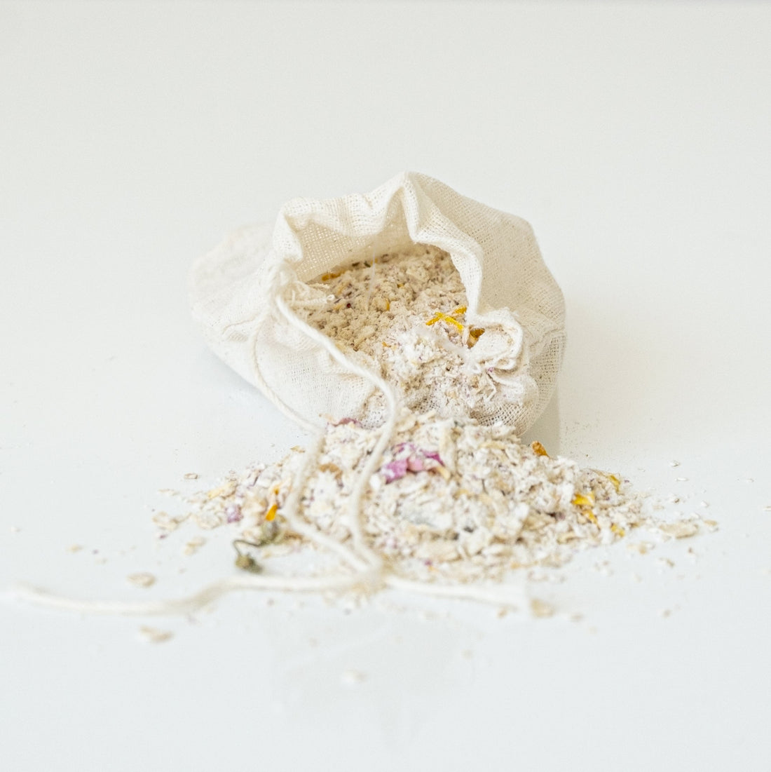 Oat bath soak blend spilling out of muslin cloth bag onto white bench.