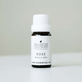 Small bottle of rose essential oil on white bench with soft grey background. 