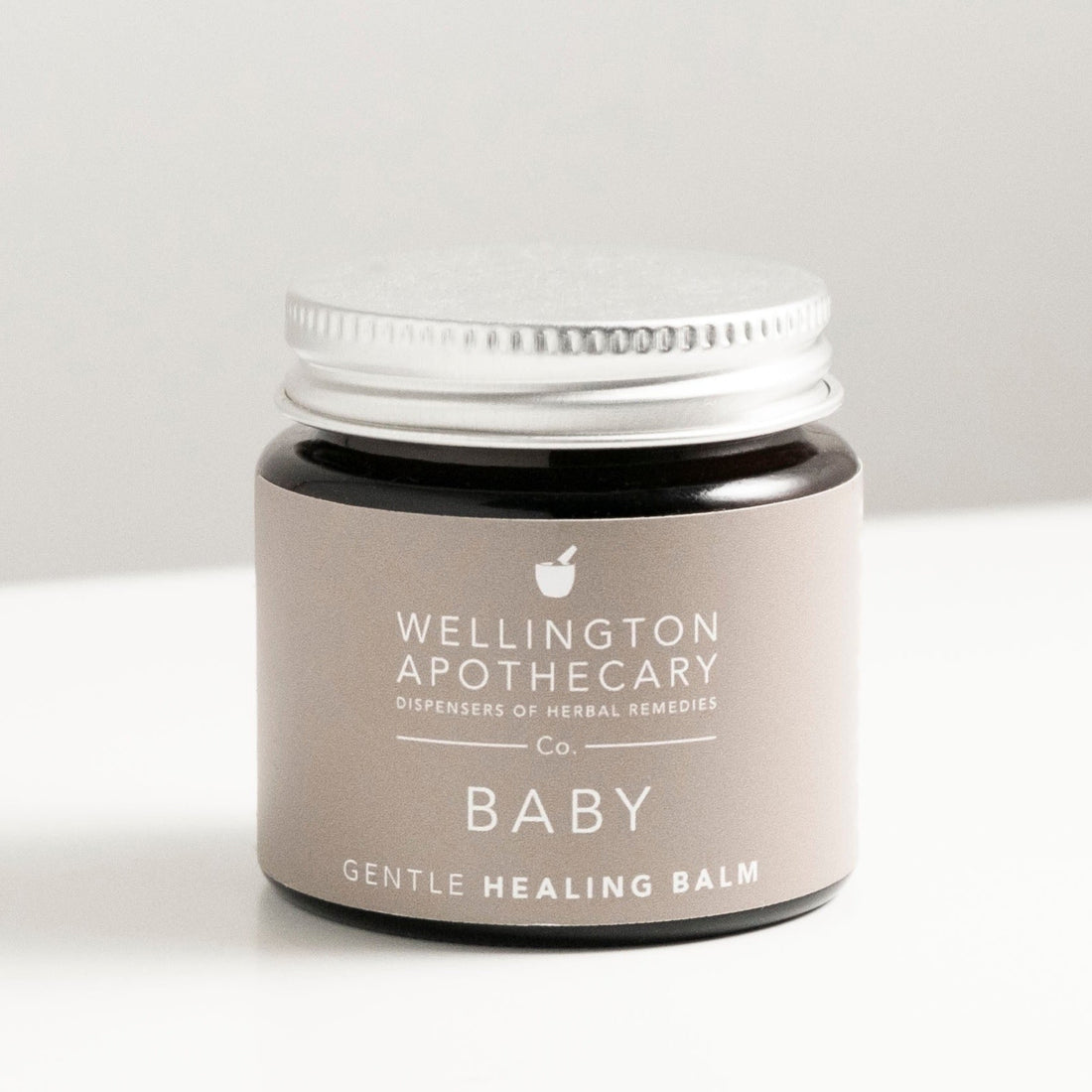 Amber glass jar of baby healing balm on white bench.
