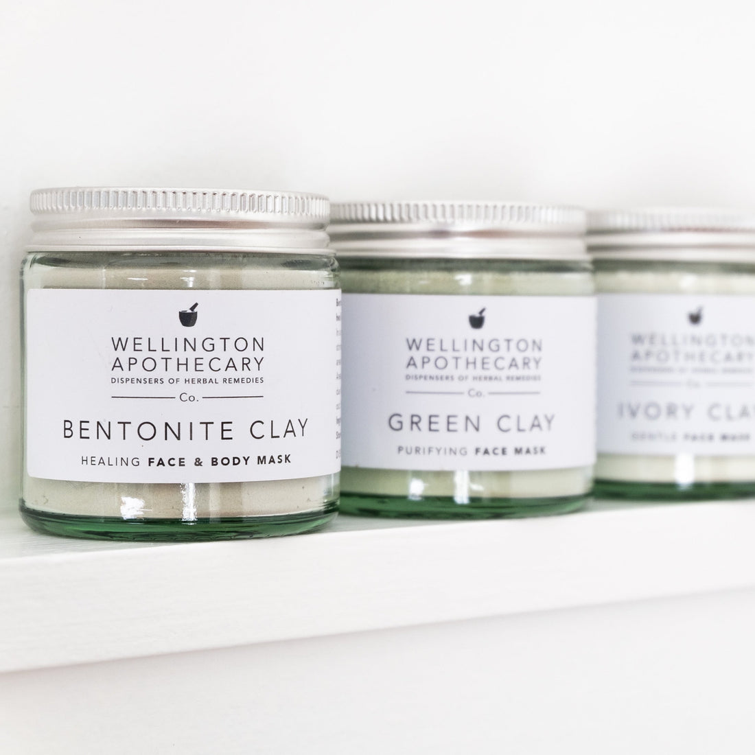 A row of glass jars containing clay powders, the first one that is in focus is bentonite clay.