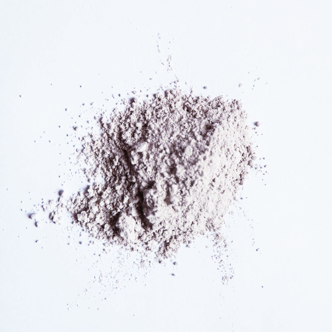 A small pile of grey bentonite clay powder on white surface.