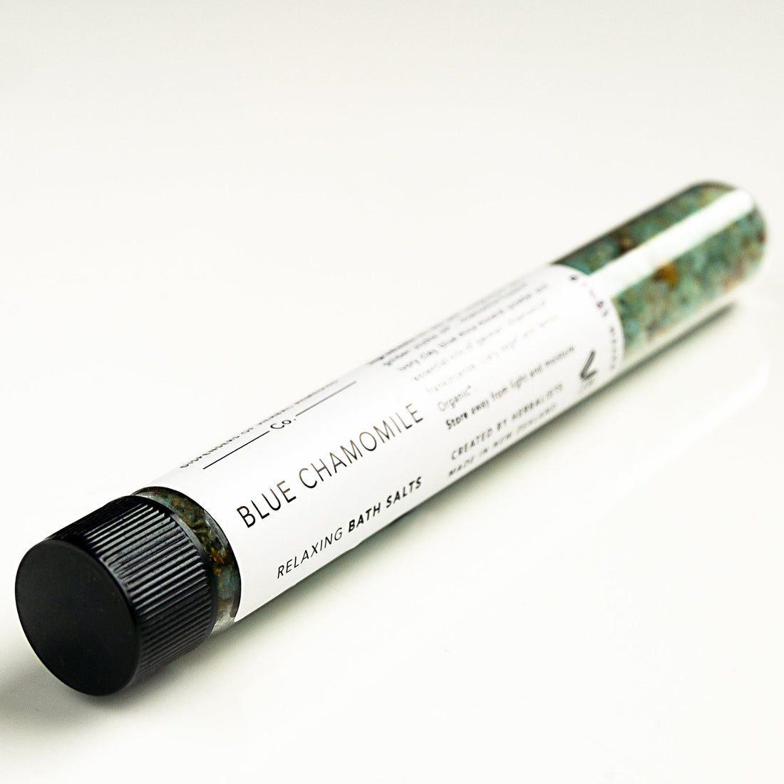 A glass test tube of blue chamomile bath salts on white surface. 