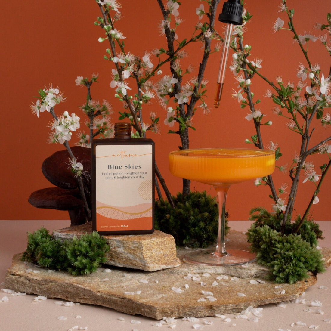 A bottle of Blue Skies tonic being dropped into an orange coloured cocktail. 