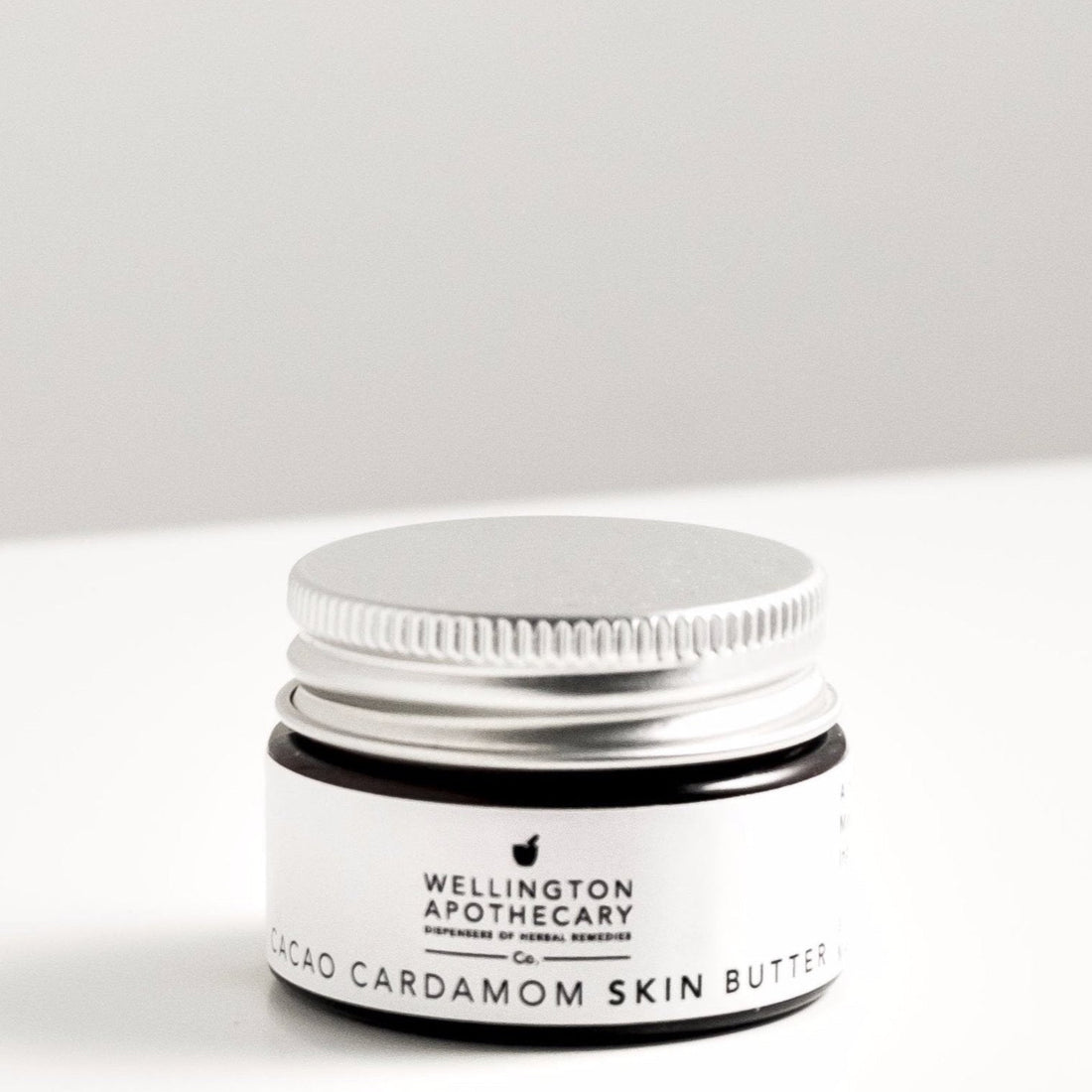 Small amber glass jar of cacao and cardamom lip balm on white bench. 