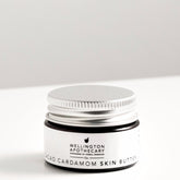 Small amber glass jar of cacao and cardamom lip balm on white bench. 