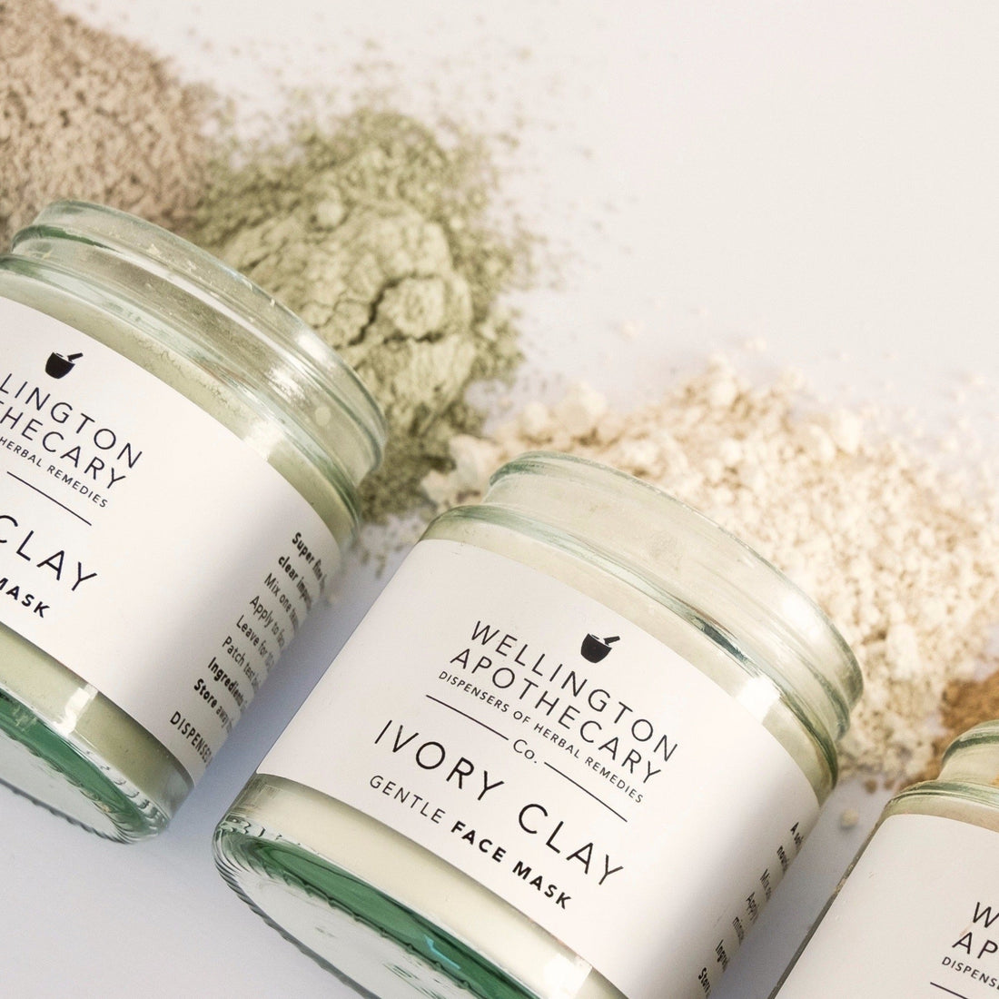 Glass jars of various coloured clay powders poured open on their sides onto a white bench.