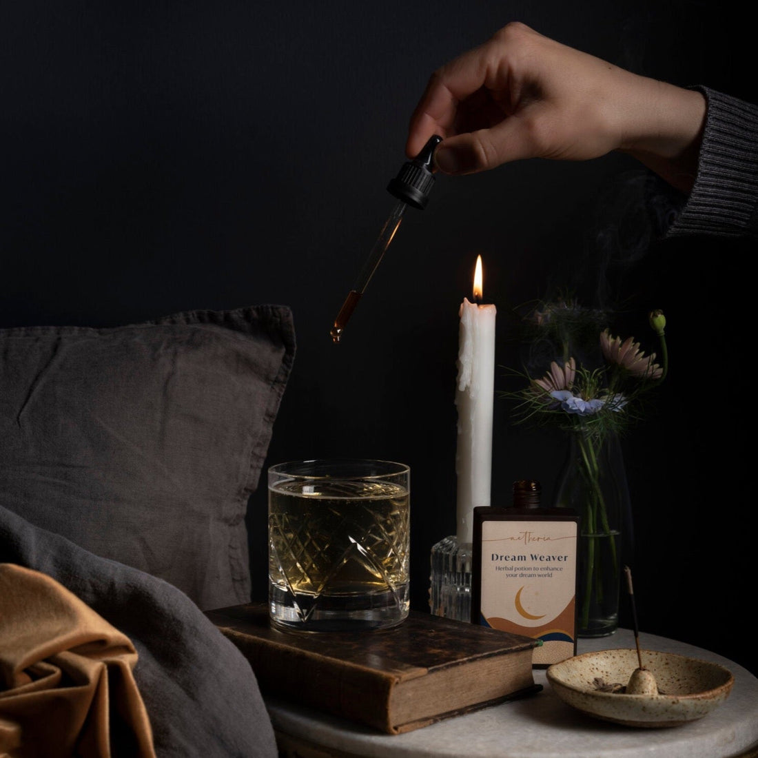 A bottle of Dream Weaver tonic being dropped into a crystal glass by a bed. 
