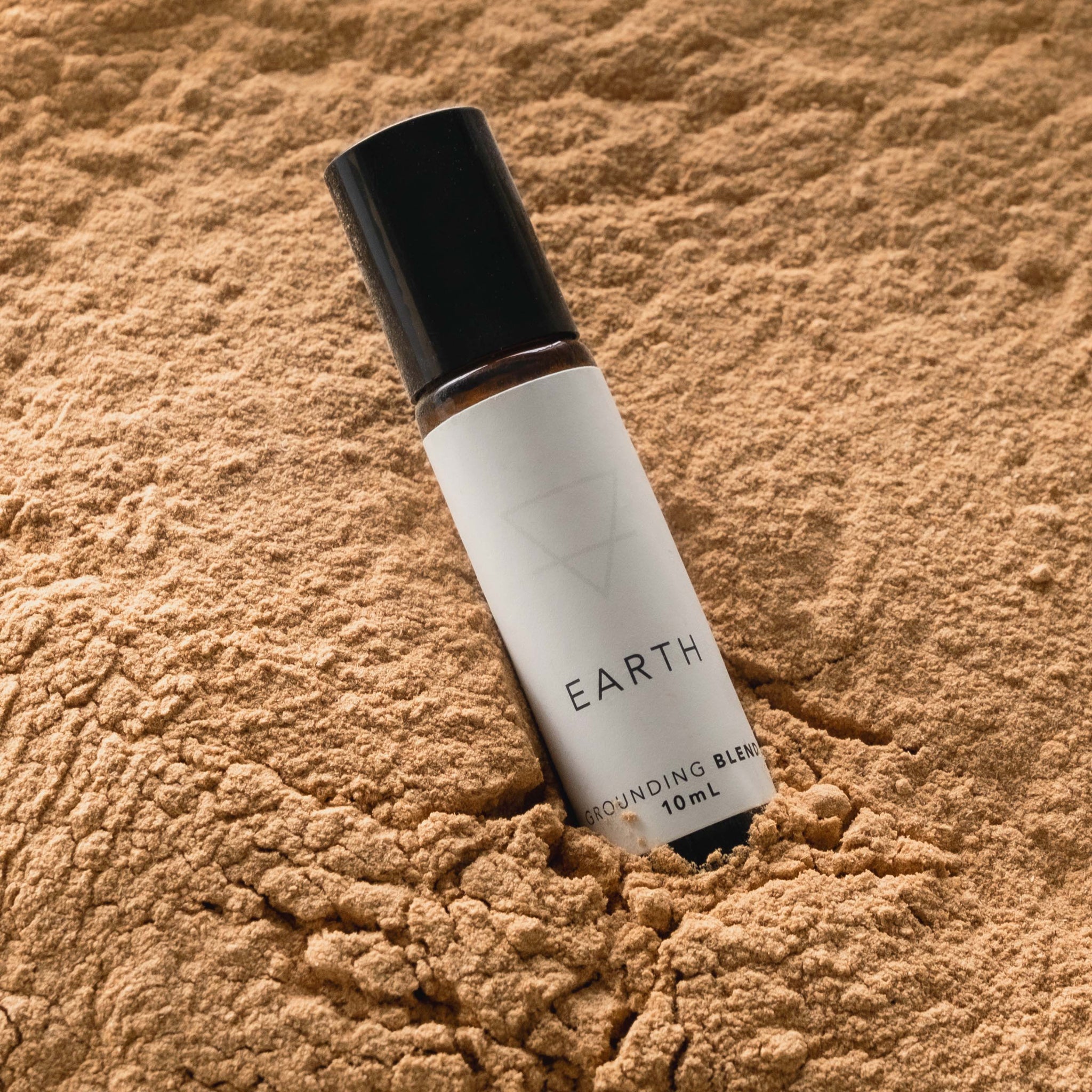 A small amber glass bottle of the Earth blend perfume oil sitting on a bed of sandalwood powder. 