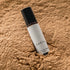 A small amber glass bottle of the Earth blend perfume oil sitting on a bed of sandalwood powder. 