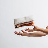 Three linen eye pillows thrown in the air, one sand, one petal and one clay. 