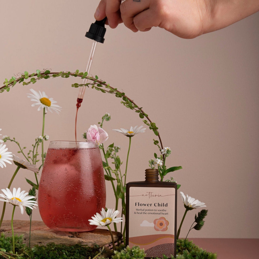A bottle of Flower Child tonic being dropped into a glass of deep pink juice. 