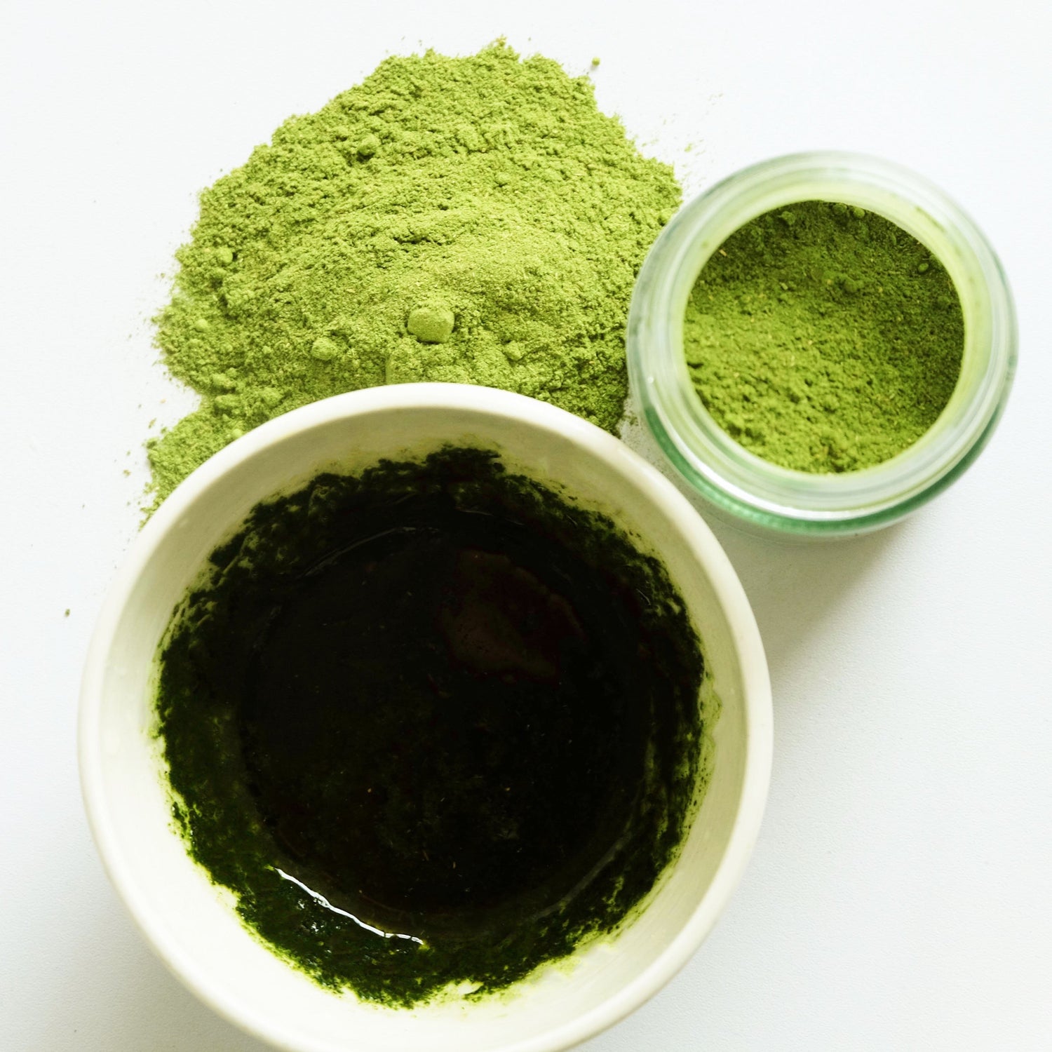 An aerial view of green herbal powders in a jar and mixed in a ceramic cup. 