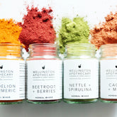 Glass jars spilling out colourful herbal powders onto a white surface. 