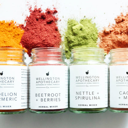Glass jars spilling out colourful herbal powders onto a white surface. 