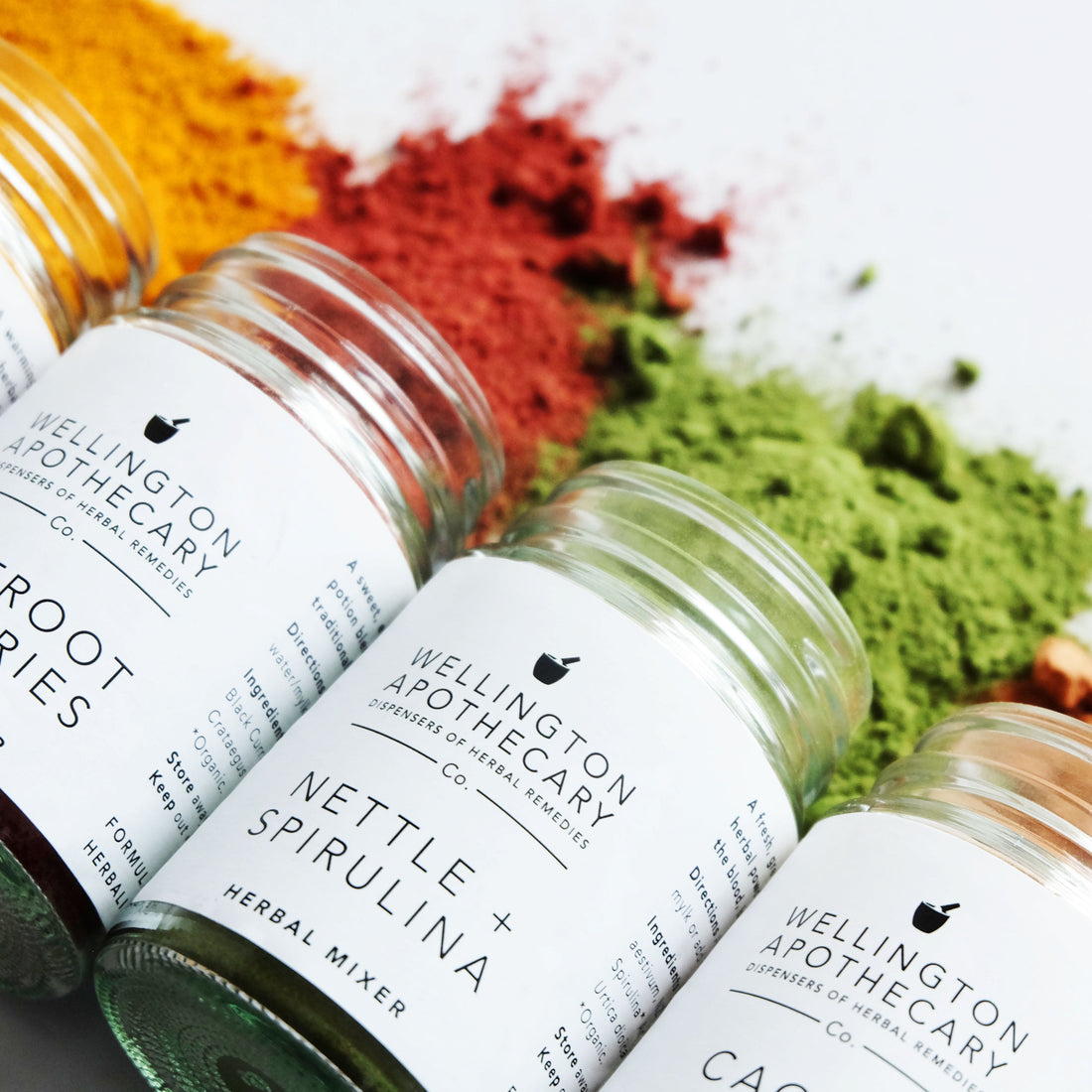 A range of colourful herbal mixers all spilling out of their glass jars onto a white surface. 