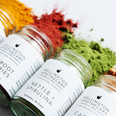 A range of colourful herbal mixers all spilling out of their glass jars onto a white surface. 