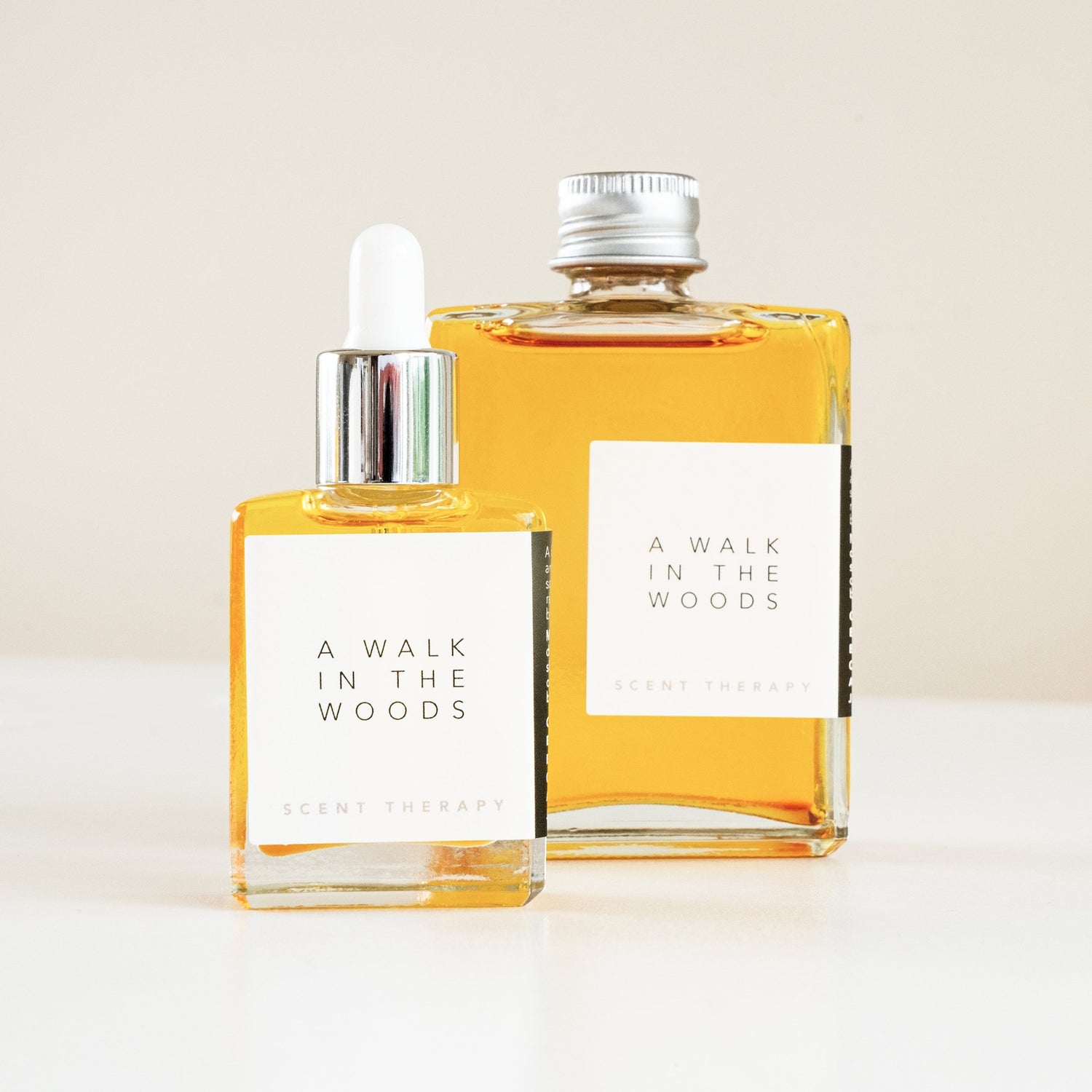Two square glass bottles, one 15mL with a dropper top and one 60ml with an aluminium lid, containing the scent therapy blend - a walk in the woods.