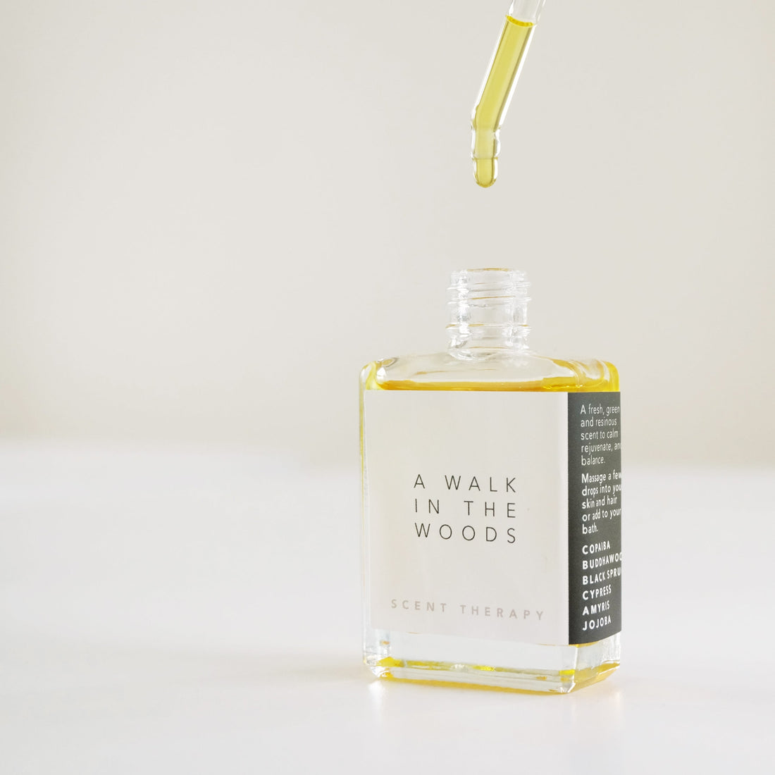A square glass bottle with a dropper dripping the scent therapy blend - a walk in the woods.