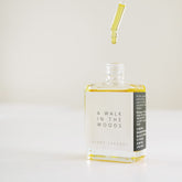 A square glass bottle with a dropper dripping the scent therapy blend - a walk in the woods.