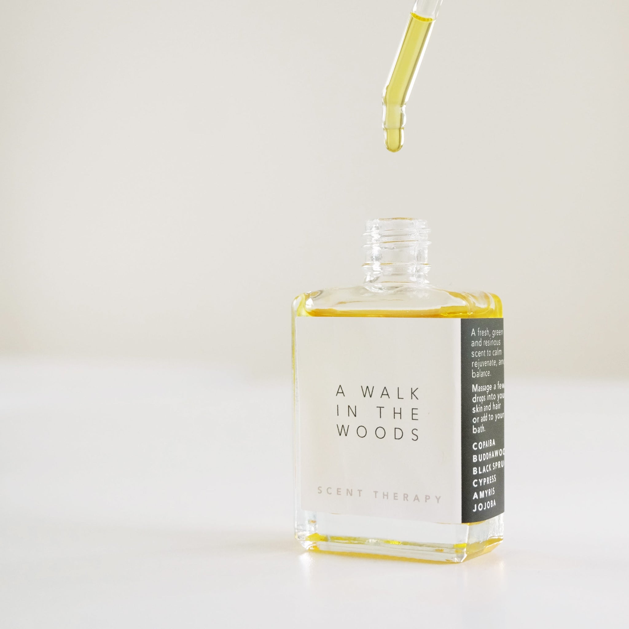 A square glass bottle with a dropper dripping the scent therapy blend - a walk in the woods.