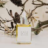 A square glass bottle with dropper top containing the scent therapy blend, a walk in the woods, with old lichen covered twigs and branches in the background.