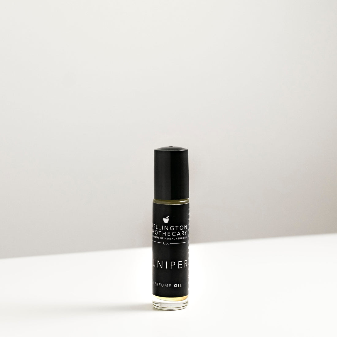 A small glass bottle of Juniper perfume oil blend on a white bench. 