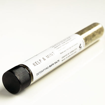 Clear glass test tube filled with kelp and mint bath salts on white bench. 