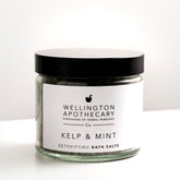 Large clear glass glass filled with kelp and mint bath salts on white bench. 