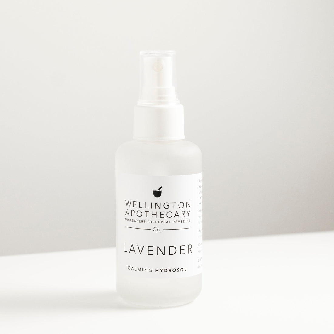 Frosted white glass spray bottle filled with lavender hydrosol on white bench.