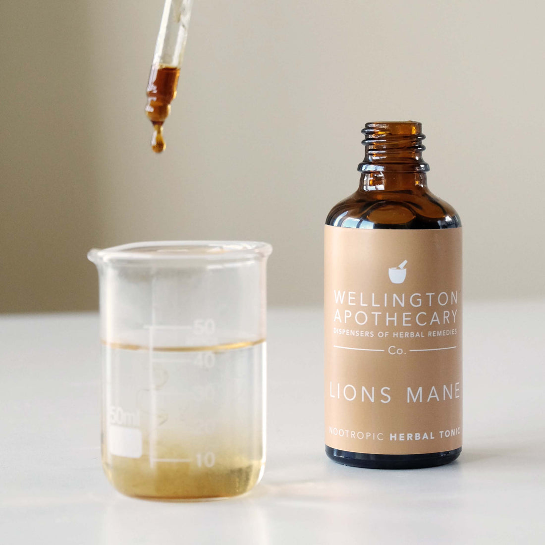 A bottle of Lions Mane tonic and a dropper top dripping it into a glass beaker. 