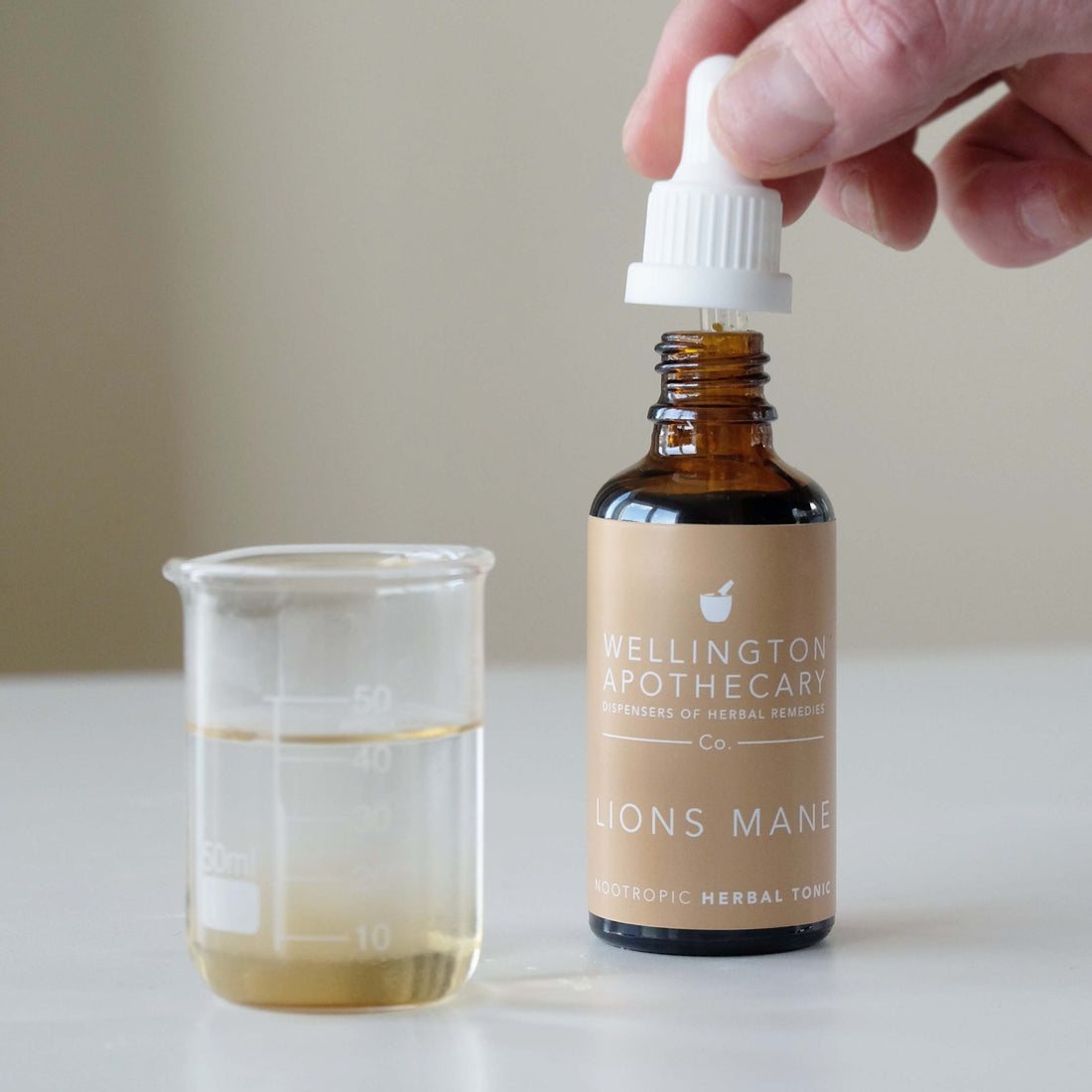 A bottle of Lions Mane tonic next to a glass beaker. 