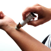 A small amber glass perfume bottle of Lunar blend being rolled onto a wrist. 
