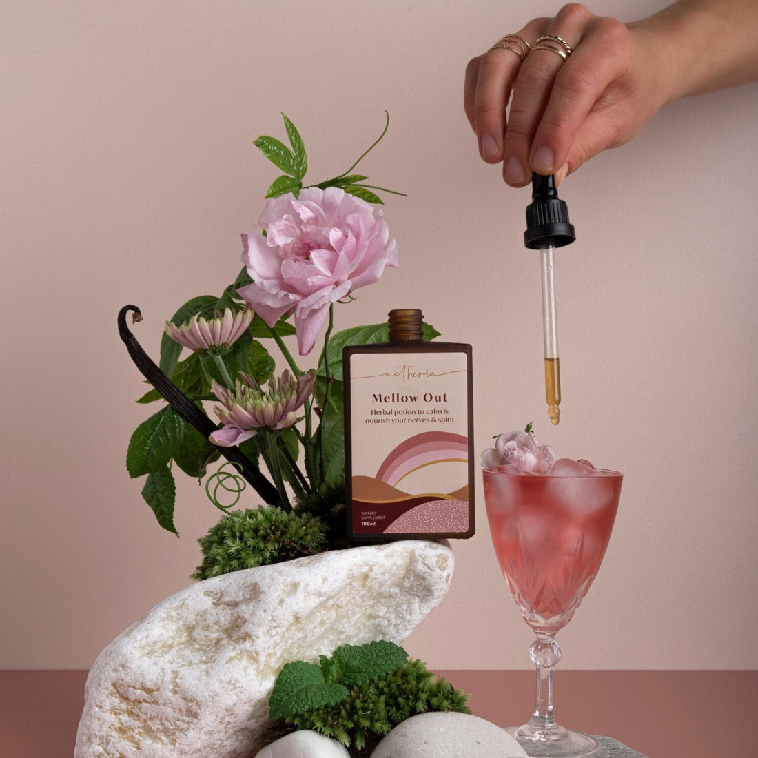 A bottle of Mellow Out tonic being dropped into a pink crystal glass.