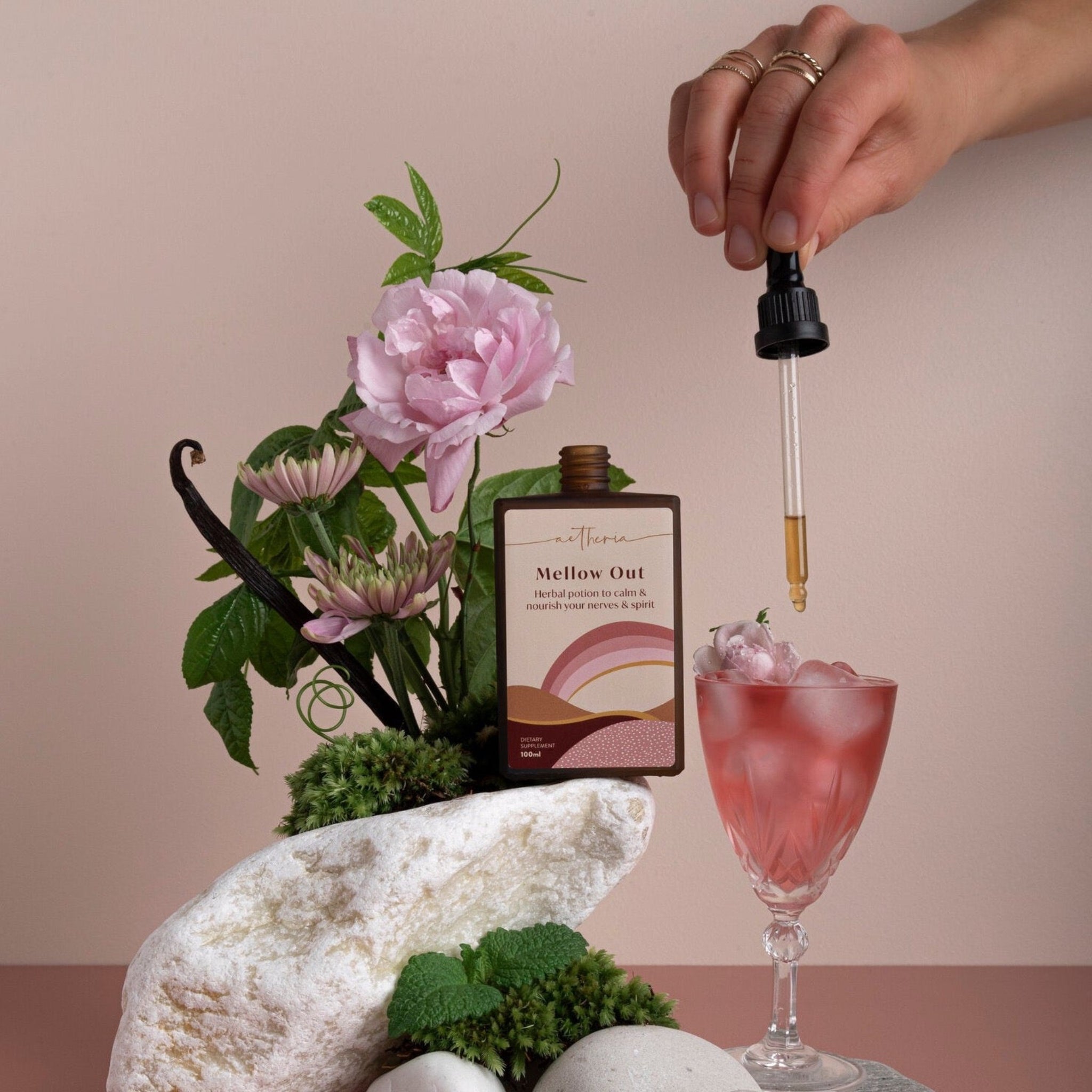 A bottle of Mellow Out tonic being dropped into a pink crystal glass.