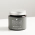 Amber glass jar with aluminium lid on white bench, labeled as muscle recovery balm. 