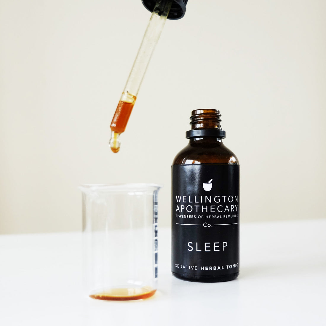 A bottle of sleep tonic with a dropper top dripping it into a glass beaker.