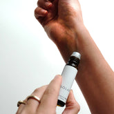 A small amber glass bottle of Solar perfume blend being rolled onto a wrist. 
