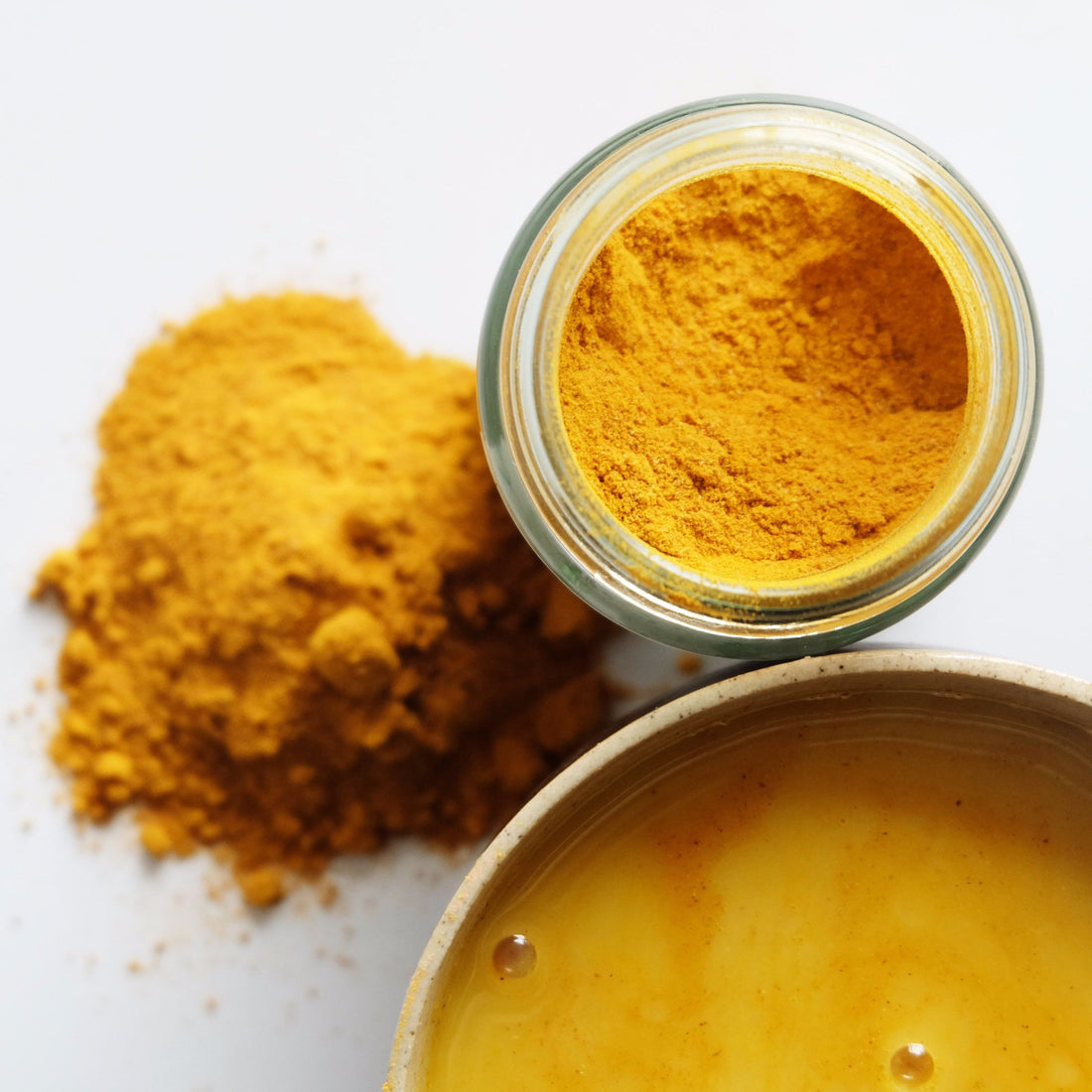 An aerial view of rich turmeric powder blend in a jar and mixed with nut milk in a ceramic mug. 
